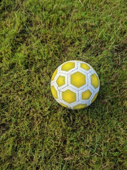 A close-up of a yellow soccer ball resting on lush green grass, perfect for sports themes.