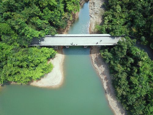 Free Drone shot of a bridge spanning a river on Hong Kong Island, surrounded by lush greenery. Stock Photo