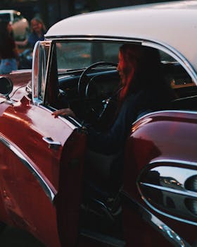 A woman sits in a glossy vintage car with chrome details during sunset.