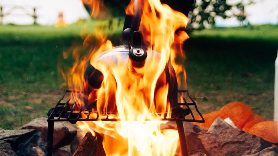 How Electric Kettles with Temperature Control Elevate Pour Over Brewing A kettle boiling over an open flame on a campfire outdoors, perfect for camping themes.