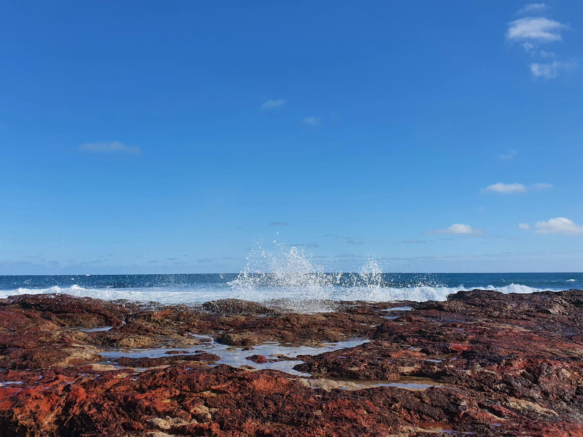 Capture of waves crashing on rocky Newhaven shore with vivid blue skies.