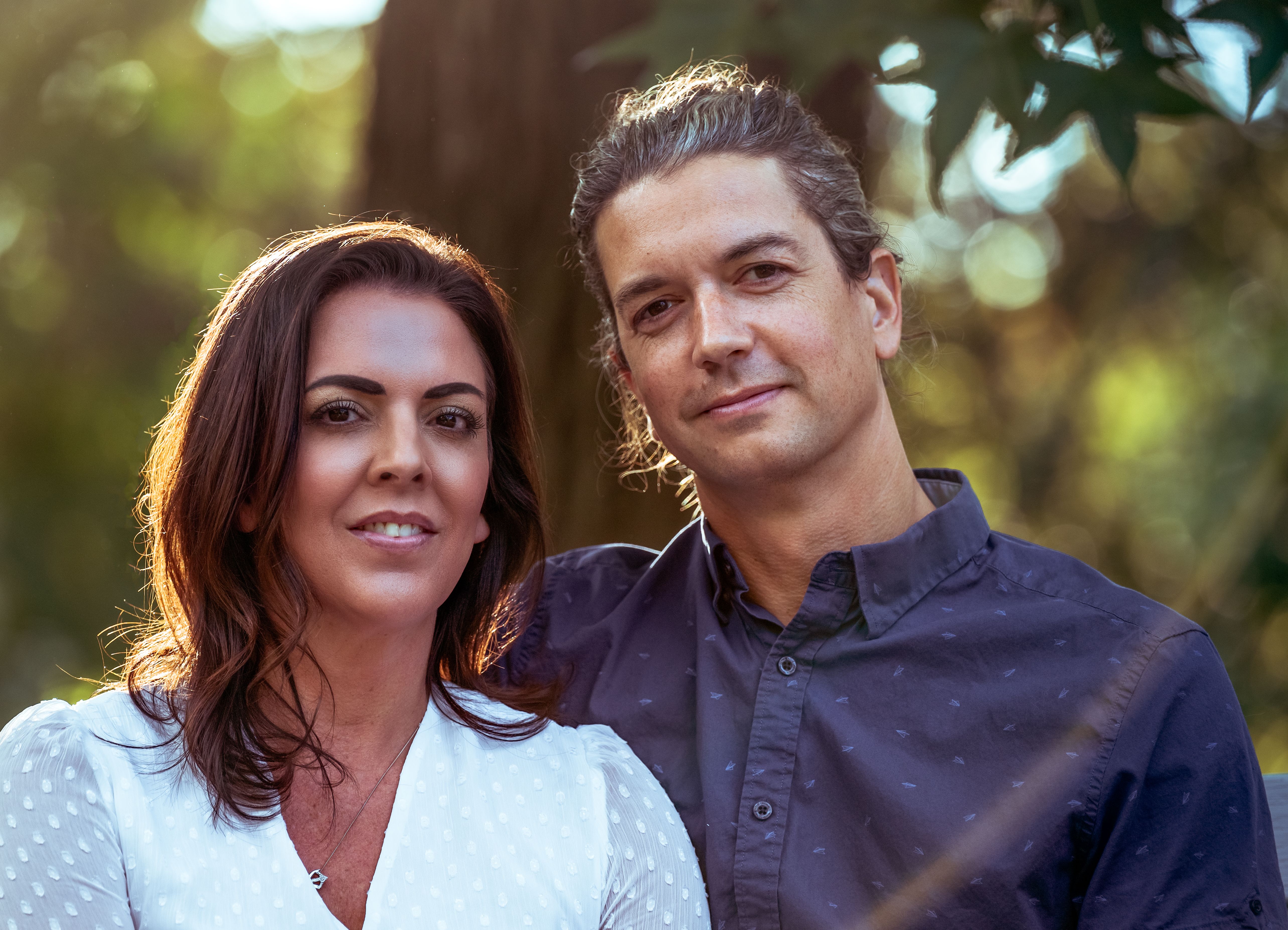 A cheerful couple posing together in a sunlit forest, exuding warmth and happiness.