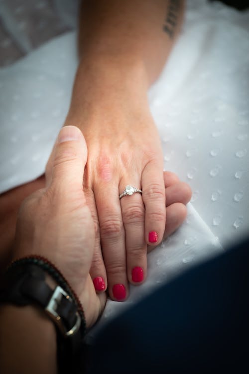 Man Holding Woman's Hand with Diamond Ring and Red Nails