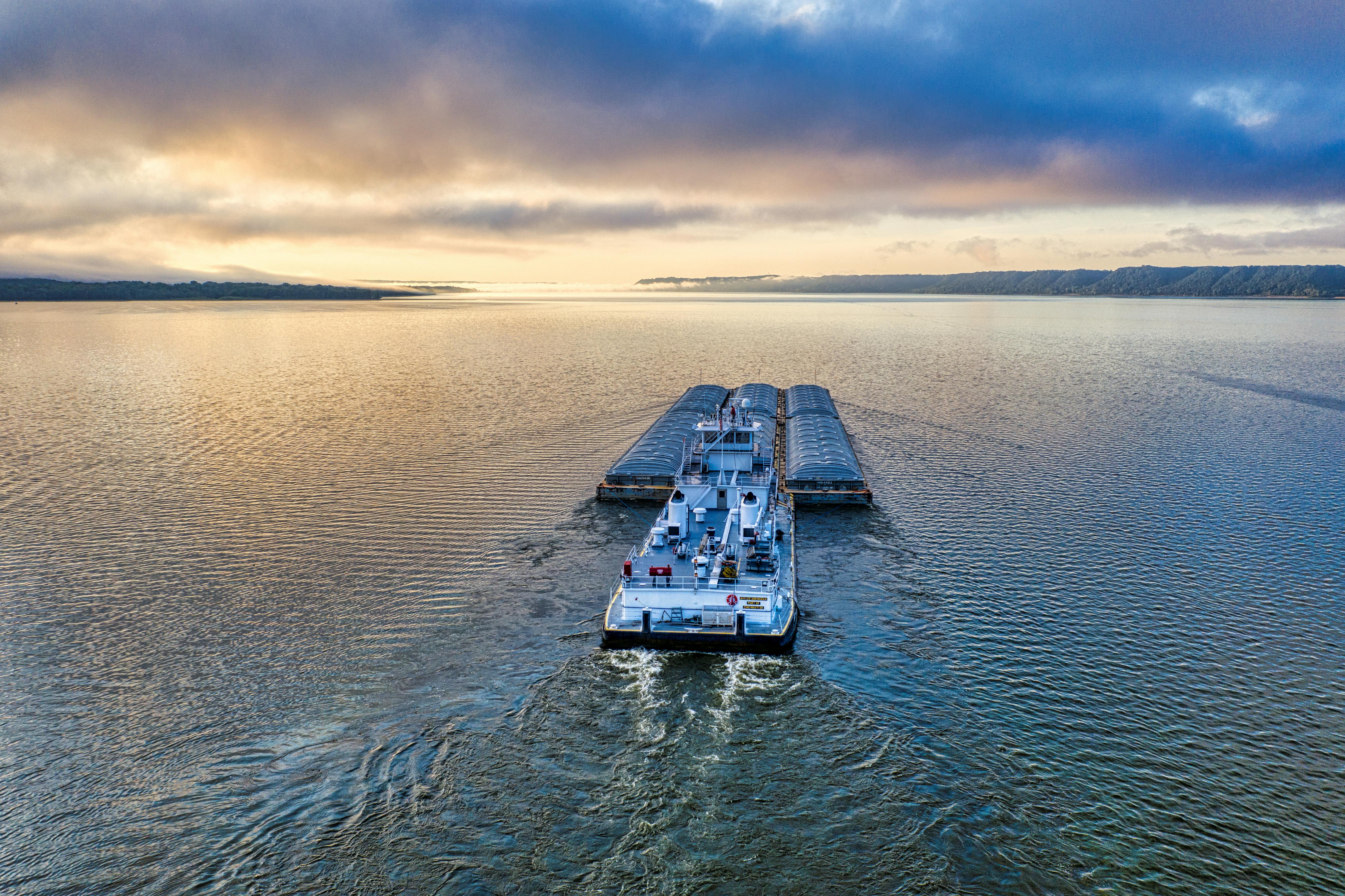 Free Aerial view of barge navigating a serene river against a colorful sunset sky. Stock Photo