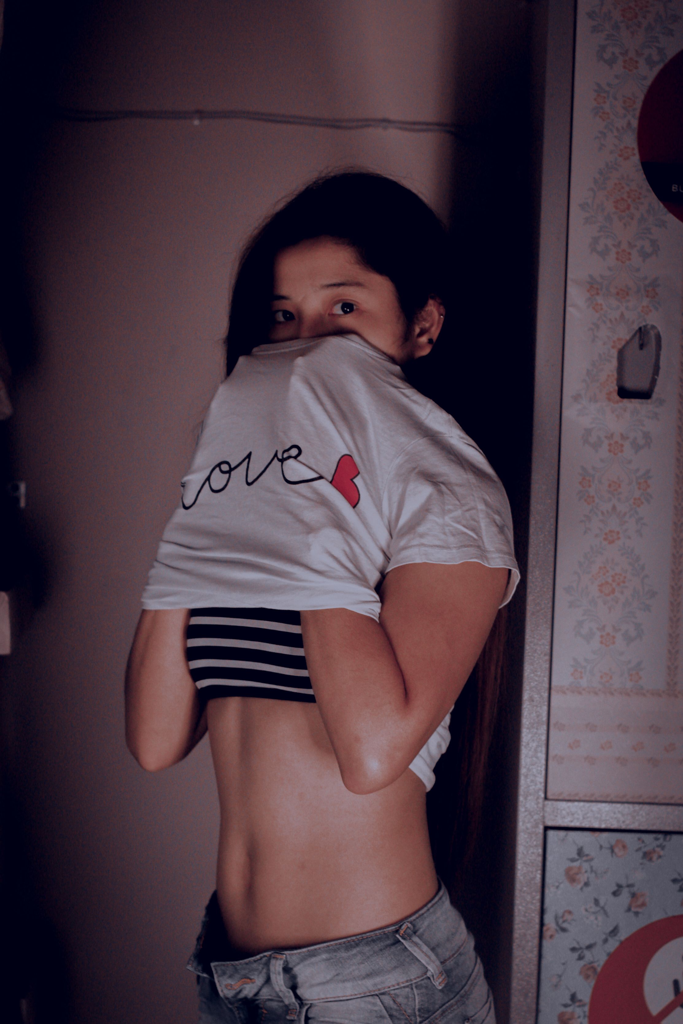 Young woman indoors lifting shirt with playful 'love' design.