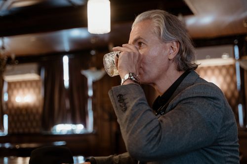 Free Profile of an elegant man with gray hair in a classic bar setting, enjoying a drink elegantly. Stock Photo