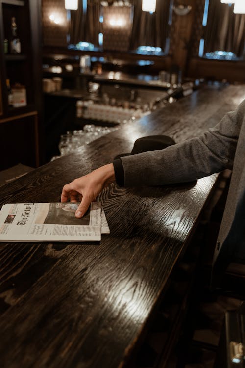 Person picking up a Newspaper on a Wooden Counter 