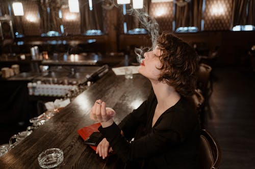 Woman in Black Long Sleeve Dress Smoking at the Bar