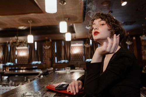 Free A fashionable woman with red lips sits smoking stylishly in a vintage bar. Stock Photo
