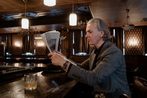 Free Mature man in formal attire enjoying newspaper at vintage bar counter with ambient lighting. Stock Photo