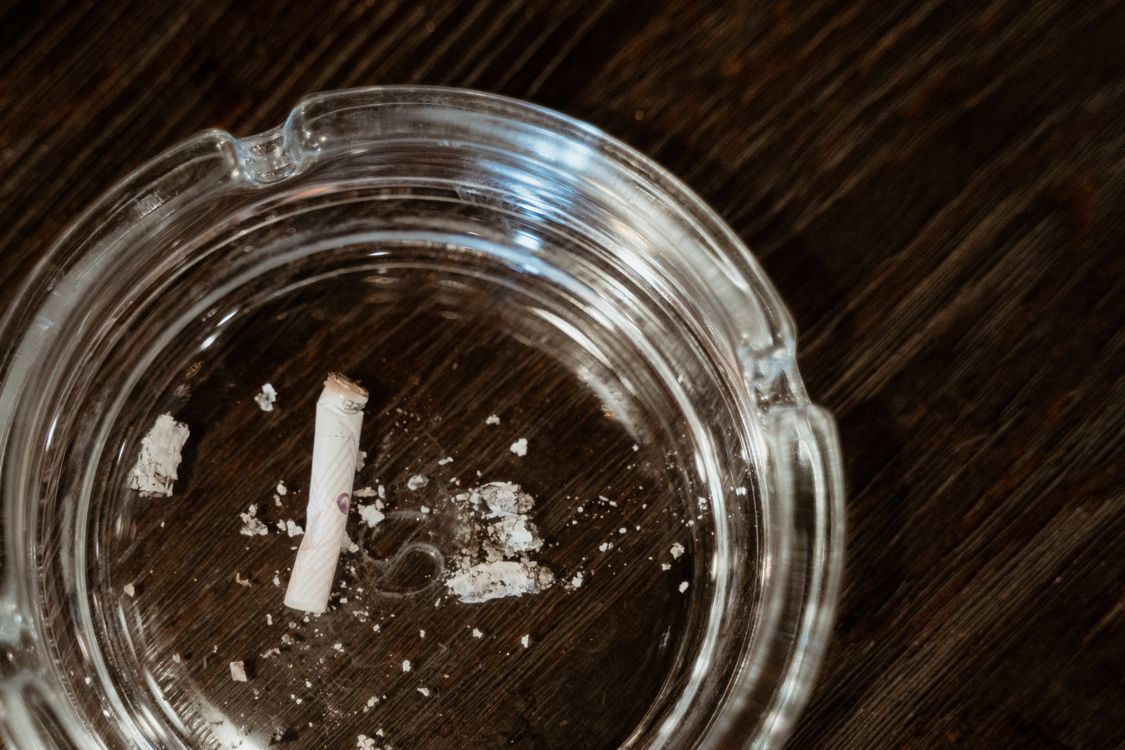 Krupni plan opuška cigarete u staklenoj pepeljari na drvenom stolu