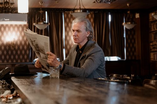 Free A senior man in a gray suit reads a newspaper at a bar, setting a classic, contemplative mood. Stock Photo