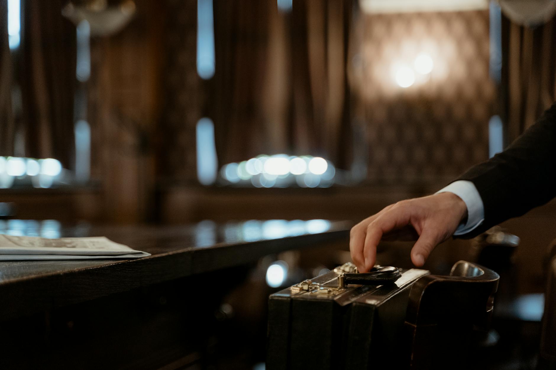 Why You Should Join My Advisers to Boost Your Financial Blog Reach 4 A close-up shot captures a hand holding a black briefcase in a dimly lit elegant room with a blurred background.