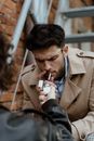 Photo of a Man in a Beige Coat Lighting a Cigarette