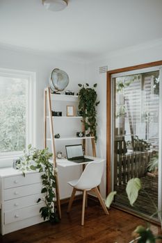 Stylish home office setup with a laptop, shelves, and lush green plants by the window.