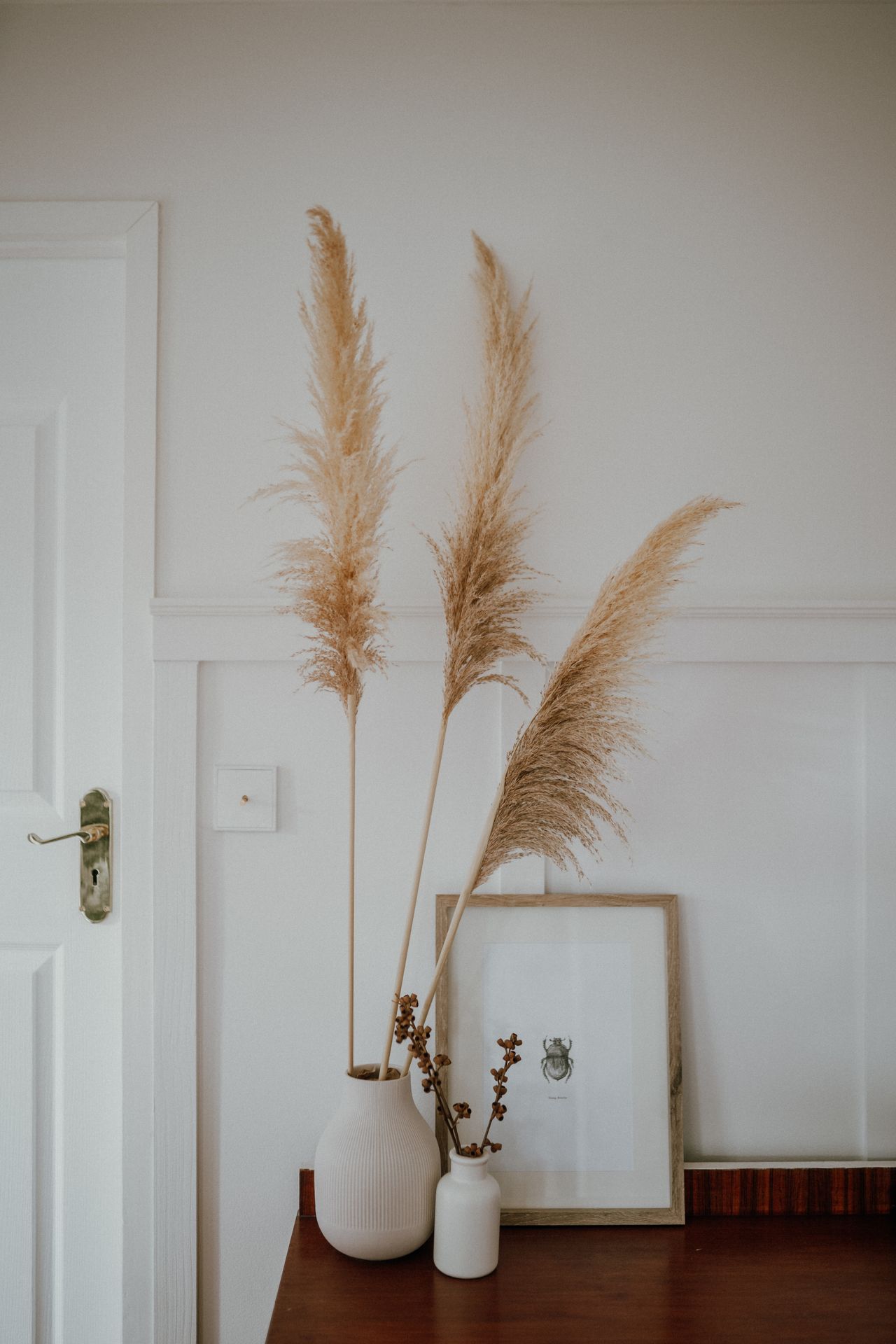 Three tall dried pampas grass stems in a white ribbed vase on a wooden entryway console