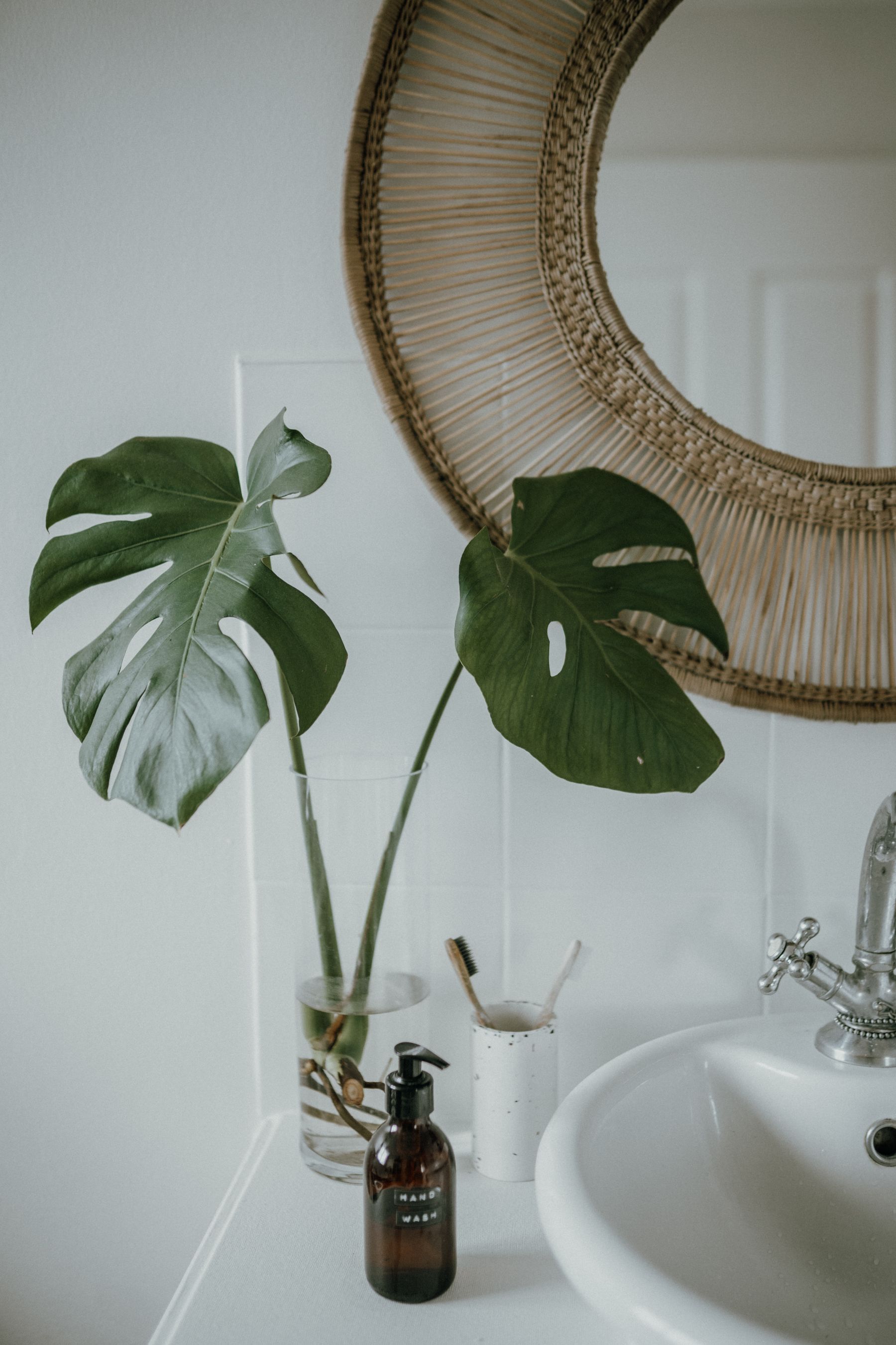 Bright boho-inspired bathroom with wicker mirror, monstera plant, vessel sink and natural textures