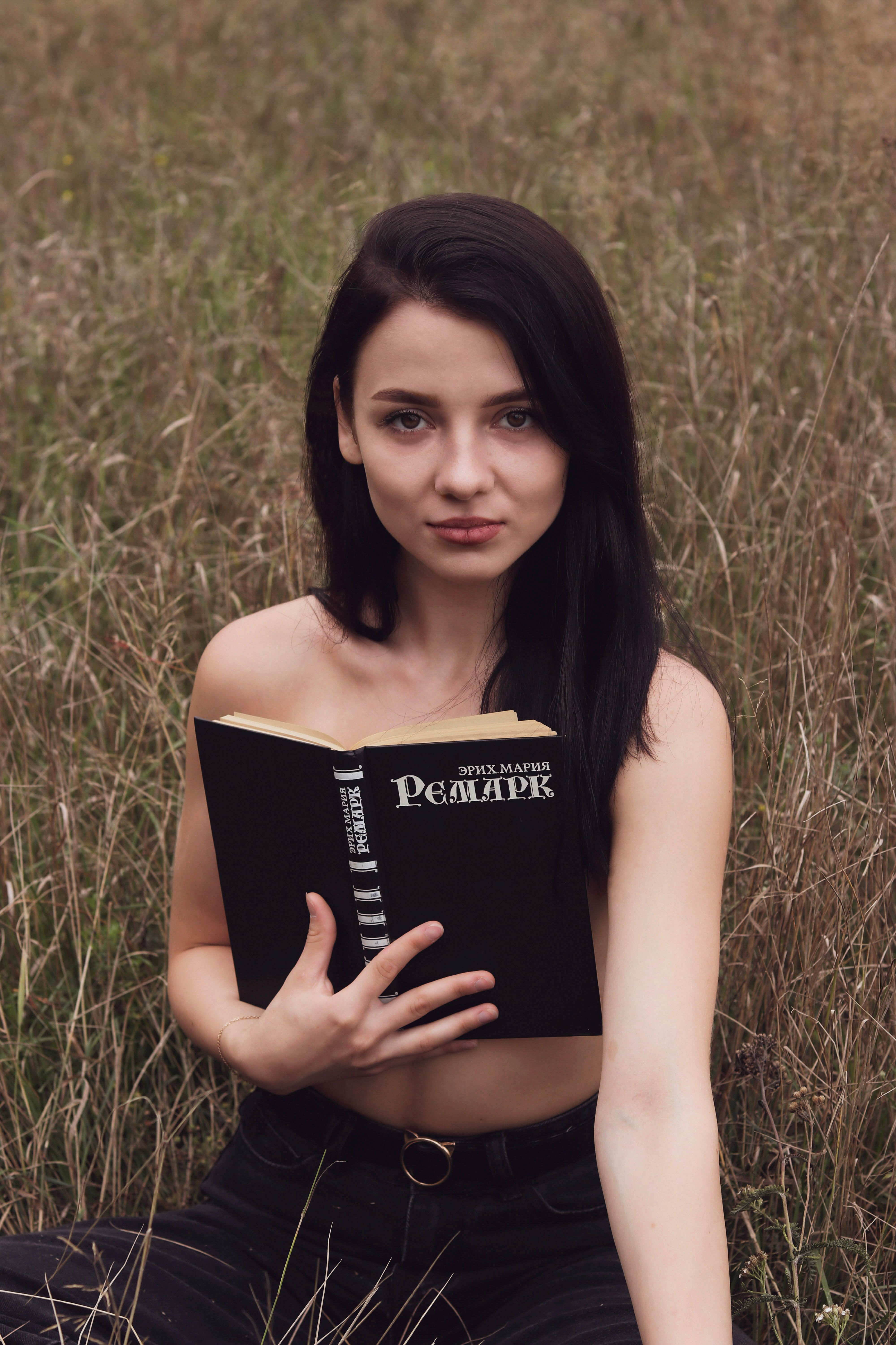 A woman sitting in tall grass holding a book by Erich Maria Remarque.