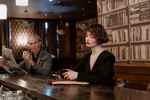 A stylish woman and man sitting at a bar reading and relaxing in a retro setting.