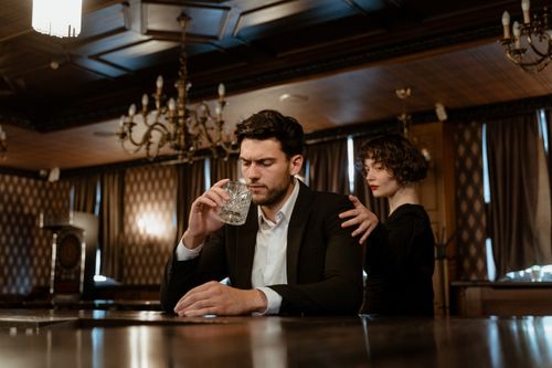 Free An elegant bar scene with a thoughtful man holding a glass and a woman comforting him. Stock Photo