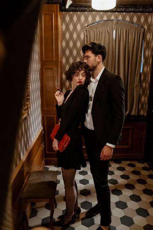 Photo of a Man in a Suit Standing Behind a Woman in a Black Dress