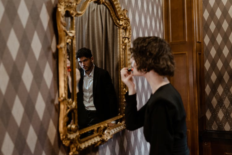 Photo Of A Man Looking At A Woman Putting On Lipstick