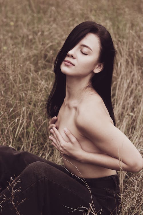 A Topless Woman Sitting on Grass Covering her Breast with Her Hands