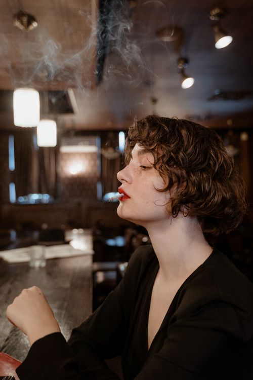 Free Stylish woman with short hair in a black top smoking indoors. Moody lighting. Stock Photo
