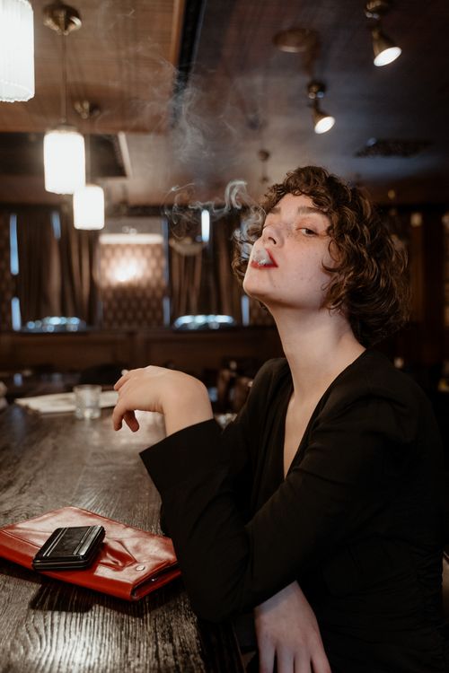 Free Caucasian woman with short hair smoking in a stylish, elegant bar setting. Stock Photo