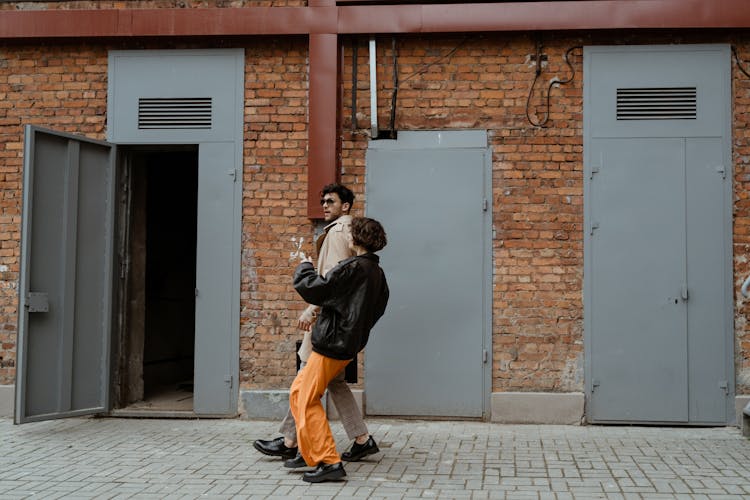 A Couple Walking Together Near Brown Brick Wall