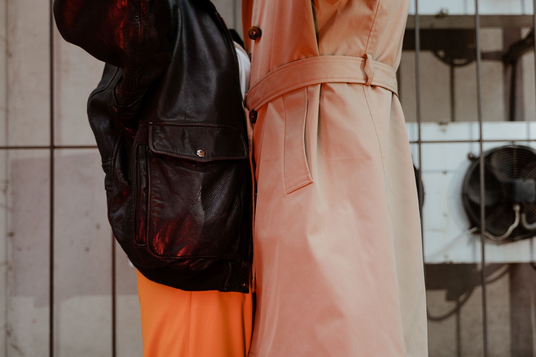 Close-up of a fashionable couple wearing leather jacket and trench coat embracing indoors.