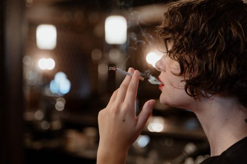 Free Close-up of a woman with short hair smoking indoors, captured in shallow focus with warm lighting. Stock Photo