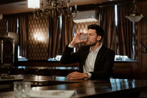 Free A man in a stylish suit sips a drink at an elegant bar setting, capturing a classic ambiance. Stock Photo