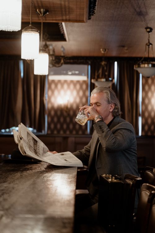 Free Man enjoying a drink while reading a newspaper at a cozy, dimly-lit bar. Stock Photo