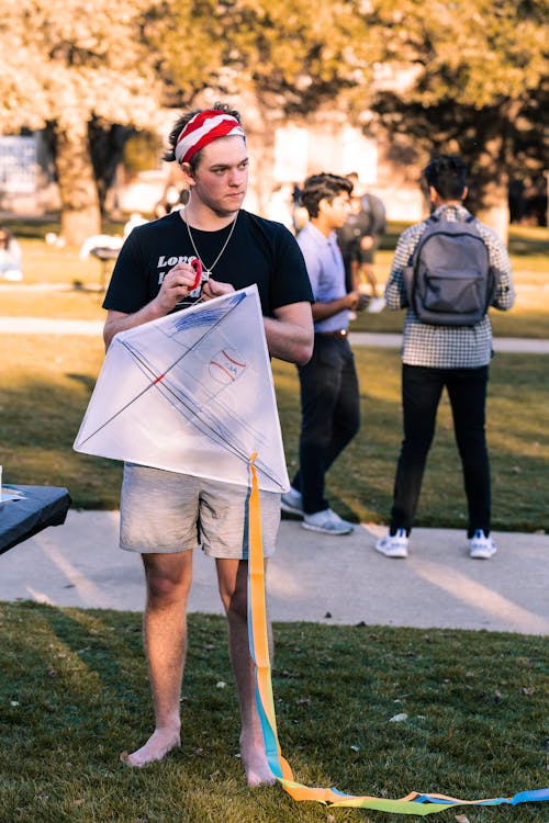 A Man with Bandana Standing on Grass Holding White Kite