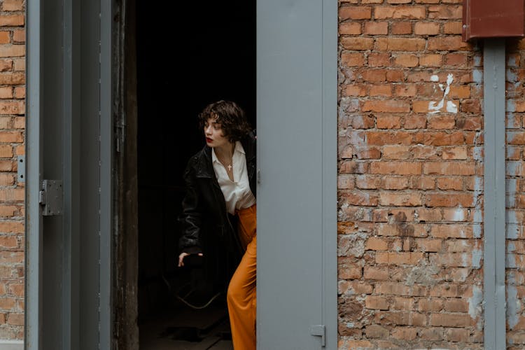 A Woman In Black Jacket Walking Out Of A Gray Doorway