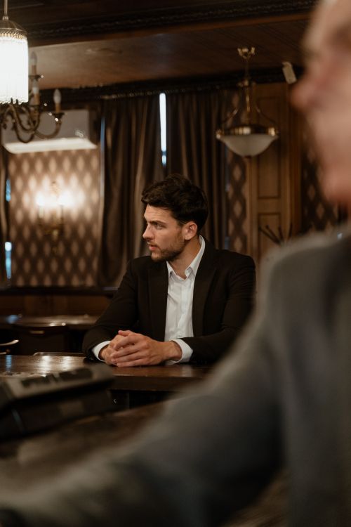 Free Stylish man in a black suit sitting at a classic bar counter, poised and thoughtful. Stock Photo
