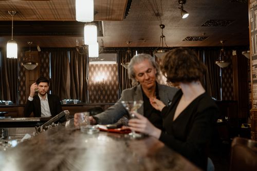 Free Three people enjoying drinks at a stylish, dimly lit bar, creating a warm atmosphere. Stock Photo