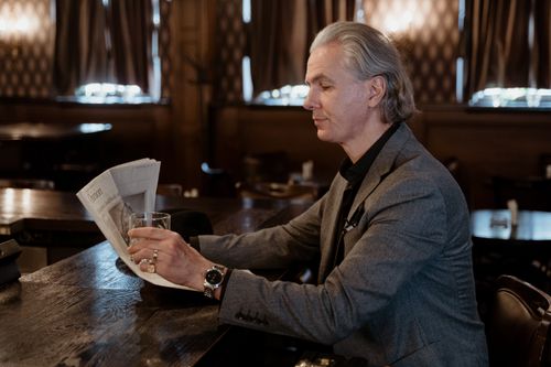Free Senior man in gray suit reads newspaper at bar, capturing a serene indoor moment. Stock Photo