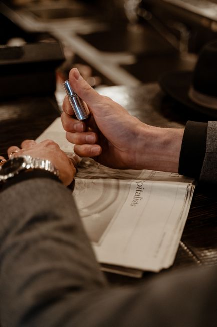 A person in a suit holds a lighter above a newspaper, creating a contemplative scene.