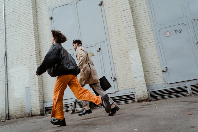 A Man And Woman Running Near A White Brick Wall