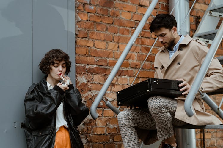 A Man Sitting On The Stairs Holding A Briefcase Beside A Woman In Black Jacket