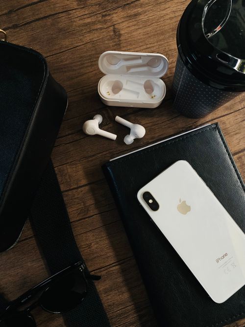 Free A stylish flat lay featuring a smartphone, earbuds, and accessories on a wooden surface. Stock Photo