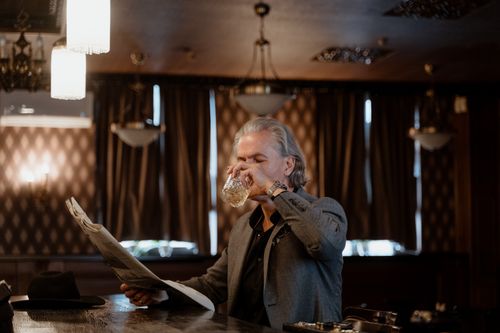 Free Sophisticated senior man reading newspaper while sipping whiskey in a dimly lit bar. Stock Photo