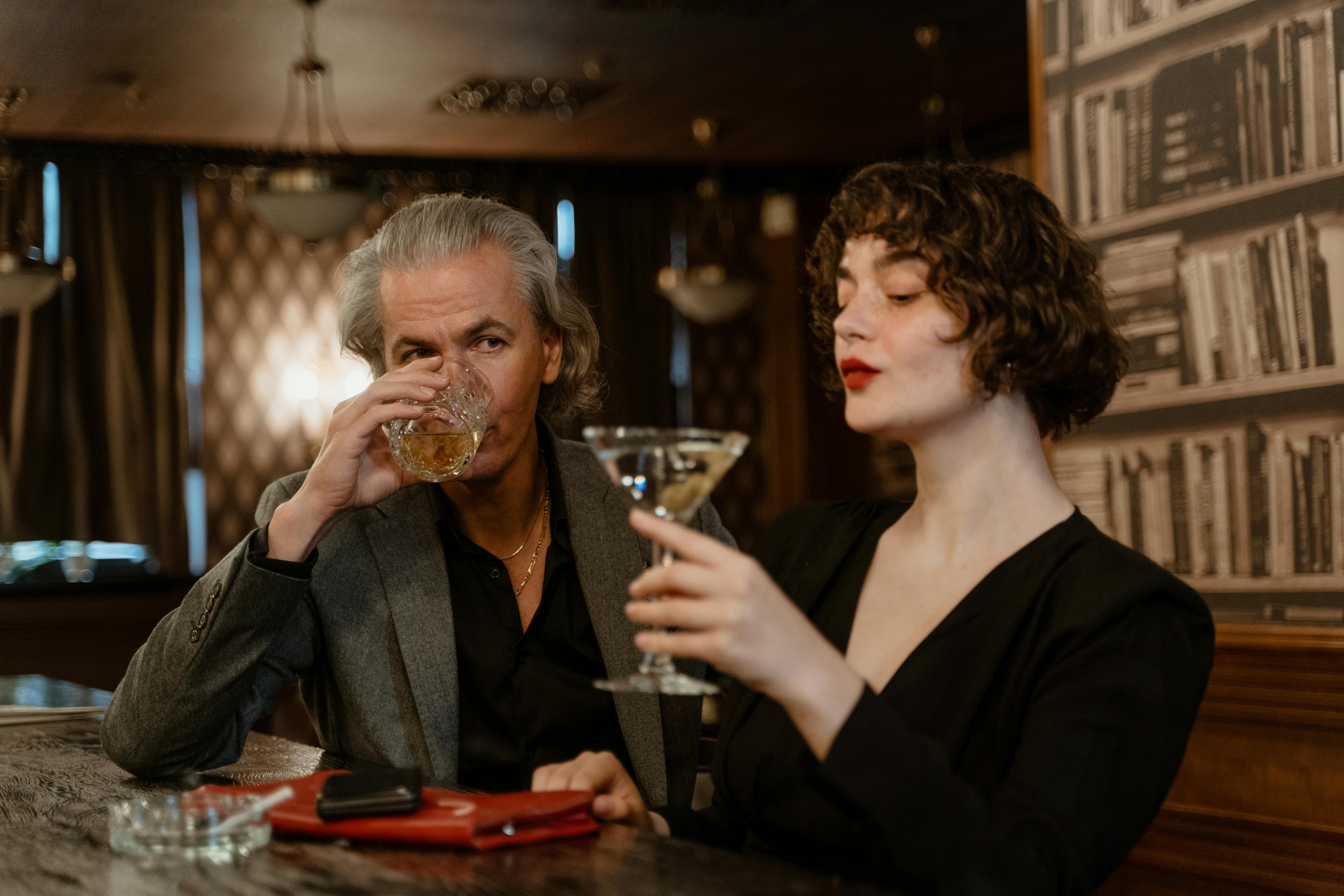 a man drinking whiskey beside a woman holding a martini glass