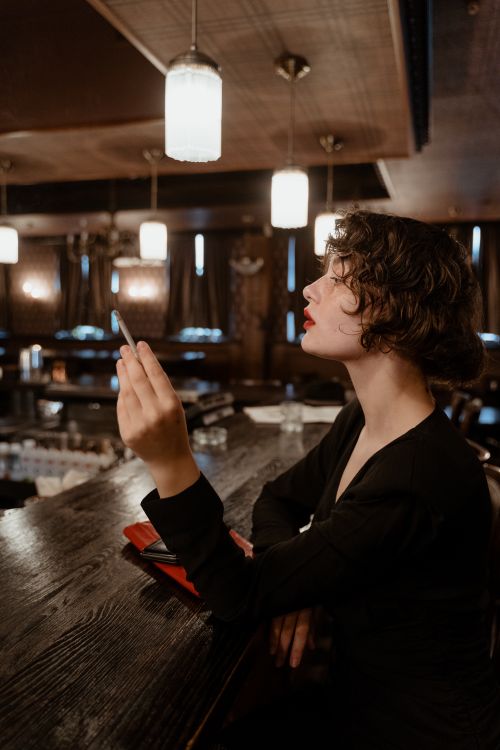 Free Side view of a fashionable woman smoking in a dimly lit bar, exuding a retro and enigmatic vibe. Stock Photo