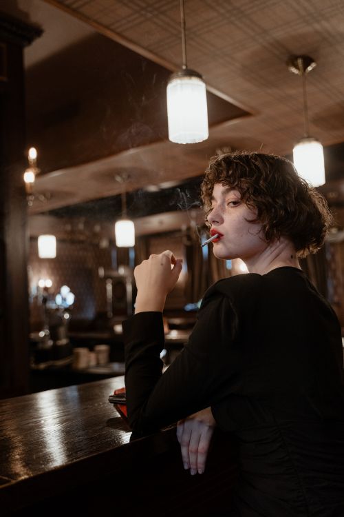 Free Stylish woman with short hair smoking in a classic bar, exuding elegance and retro charm. Stock Photo
