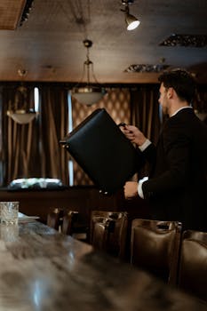 A professional man in a suit holds a briefcase in a dimly lit upscale restaurant.