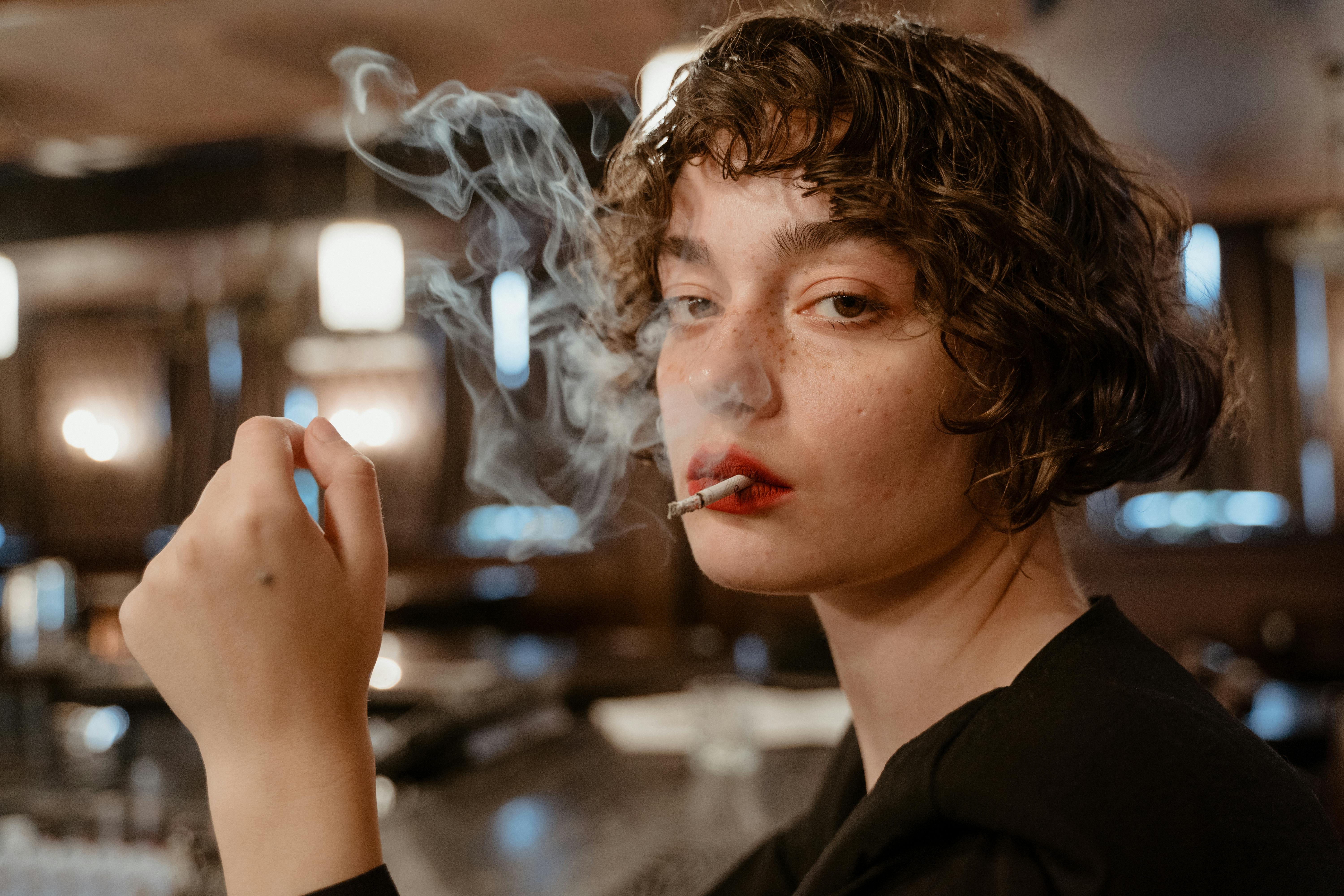 Stylish young woman with short hair smoking indoors, creating a moody atmosphere.