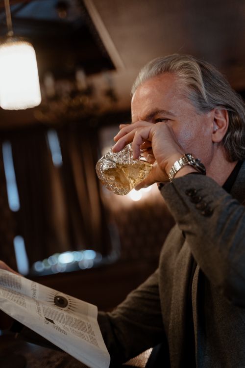 Free A mature man sips whiskey while reading a newspaper in a cozy bar setting. Stock Photo